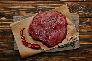 top view of fresh raw meat on baking paper with chopped chilli pepper and garlic on wooden background