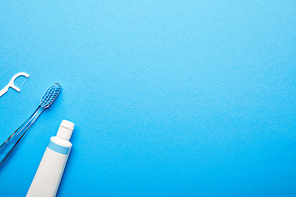top view of dental floss| toothbrush and toothpaste arranged on blue backdrop| dentistry concept