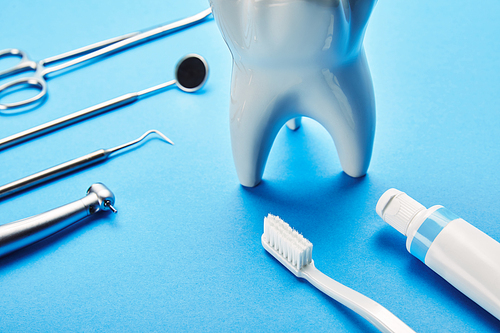 close up view of white tooth model| toothbrush| toothpaste and stainless dental instruments on blue backdrop