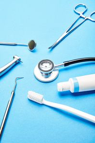 close up view of arrangement of sterile dental instruments| stethoscope| toothbrush and toothpaste on blue backdrop| dental care concept