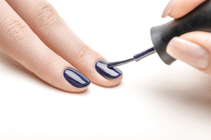 female manicurist applying navy blue nail polish on fingernail of woman on white background