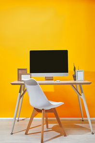 Computer| photo frames and cactus on workplace with yellow wall at background