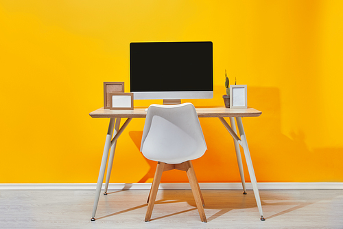 Computer| photo frames and cactus at workplace near  yellow wall