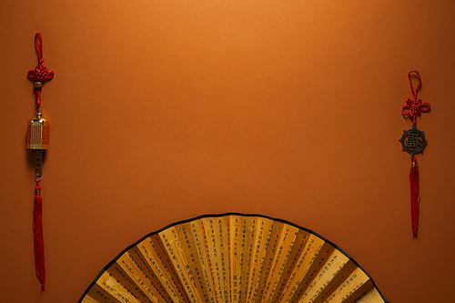 top view of golden fan with hieroglyphs and traditional chinese decorations on brown background