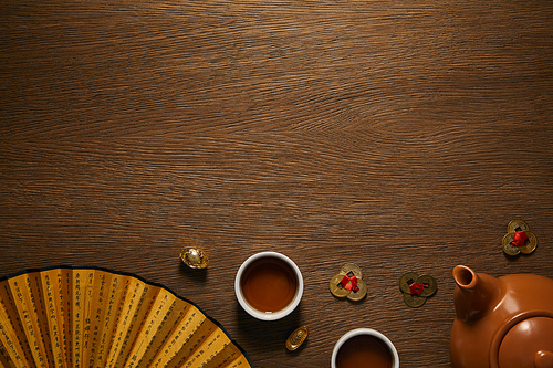 top view of tea set| fan with hieroglyphs and golden coins on wooden surface