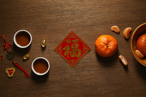 top view of fresh ripe tangerines| golden hieroglyph| cups of tea and coins on wooden surface