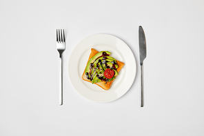 top view of toast in plate with avocado and cherry tomato| fork and knive on grey background