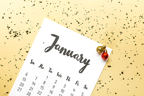 top view of january calendar and christmas baubles with golden confetti on beige background