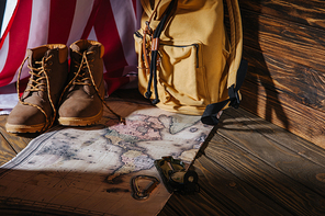 trekking boots| hiking equipment| map| backpack and american flag on wooden surface
