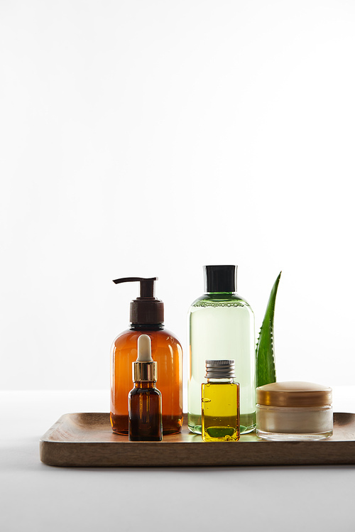 Wooden tray with various cosmetic containers and aloe vera leaf on white background