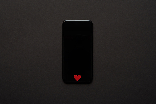 top view of smartphone with blank screen and small red heart sign on dark background