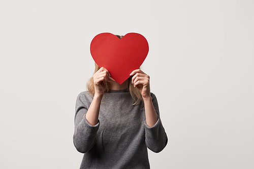 girl hiding face behind empty red paper cut heart card isolated on grey