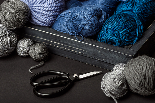 close up view of grey| purple and blue knitting clews in wooden box on grey tabletop with scissors