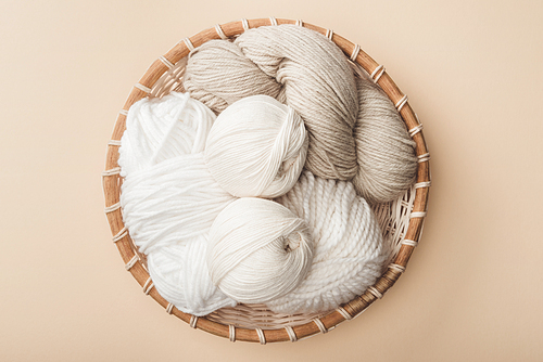 top view of white and beige yarn in wicker basket on beige background