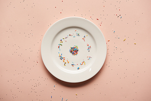 top view of white plate with sprinkles on pink background