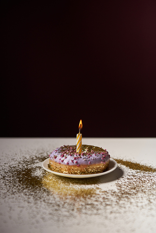 candle in middle of sweet donut with shiny sparkles on white table isolated on black