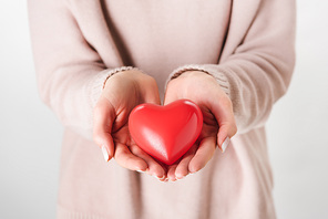Cropped view of woman in beige sweater holding toy heart