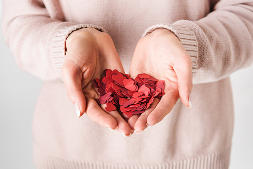 Partial view of woman in pink sweater holding paper hearts on grey background