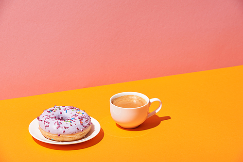 tasty donut with saucer and coffee cup on yellow surface and pink background