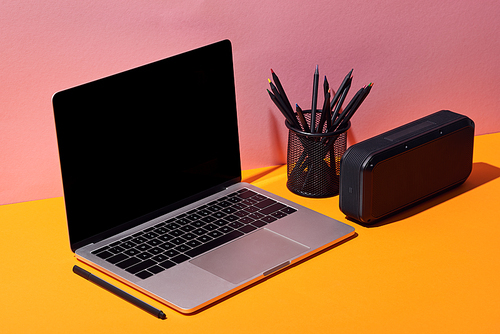 cropped view of woman using laptop with blank screen near pencil holder and speaker