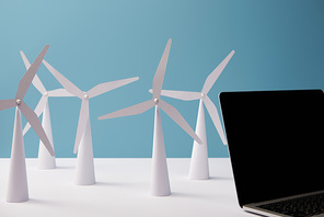 laptop on white table with windmill models on blue background