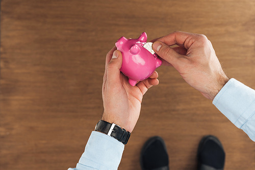 top view of man puting in pink piggy bank coin on wooden background