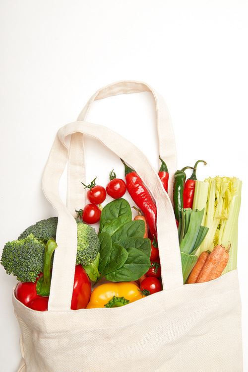 Studio shot of spinach leaves and vegetables in eco bag on white background