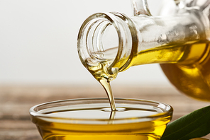 pouring olive oil from bottle into glass bowl on grey background