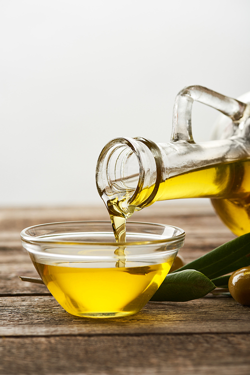 pouring oil into glass bowl| olive tree leaves and olives on wooden surface