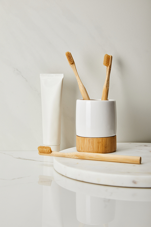 bamboo toothbrushes| holder and toothpaste in tube on white marble background