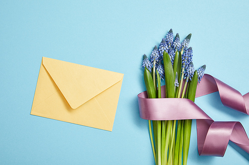 top view of yellow envelope, and blue hyacinths covered with violet satin ribbon on blue