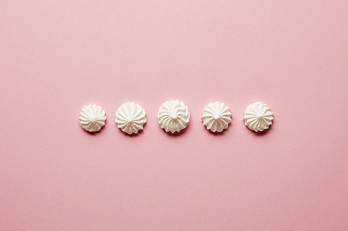 Flat lay with sweet white meringues in horizontal row on pink background