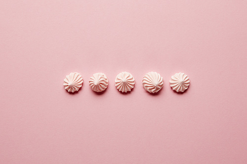 Flat lay with pink meringues in horizontal row on pink background
