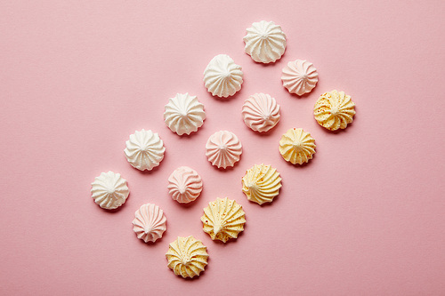 Top view of white, pink and yellow meringues in rows on pink background