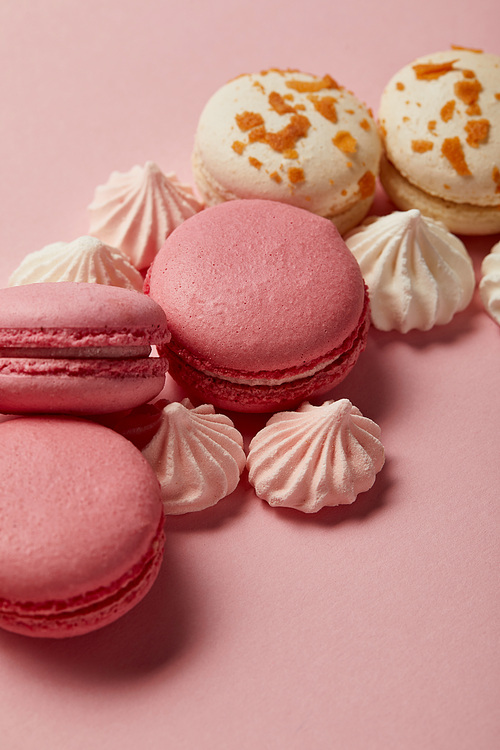 Tasty french macaroons with meringues on pink background