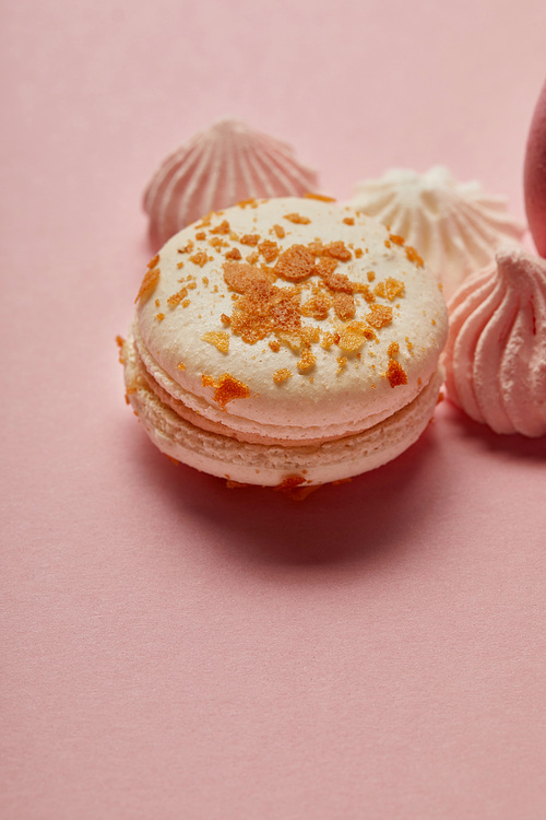 White macaroon with yellow pieces and meringues on pink background