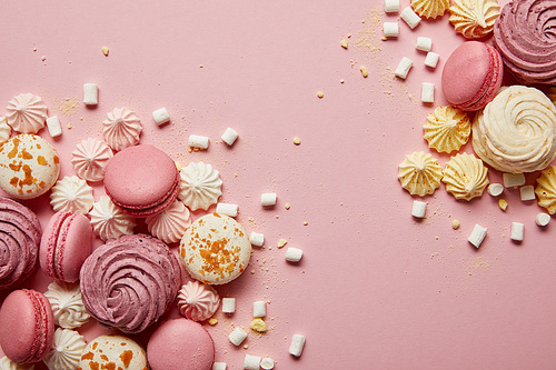 Top view of delicious sweet macaroons, meringues and marshmallows with yellow pieces on pink background