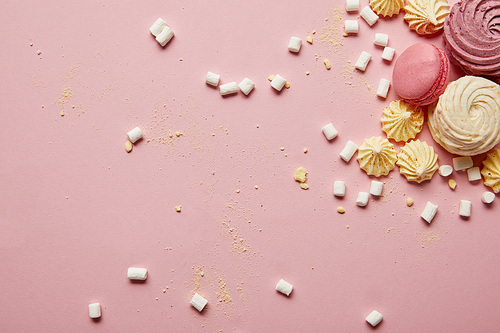 Top view of sweet pink macaroons, meringues and marshmallows with yellow pieces on pink background