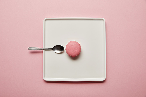 Top view on pink macaroon with teaspoon on white square dish on pink background