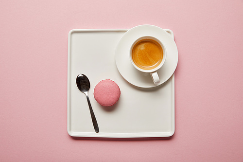 Top view of pink macaroon with spoon and cup of coffee on big square white dish on pink background