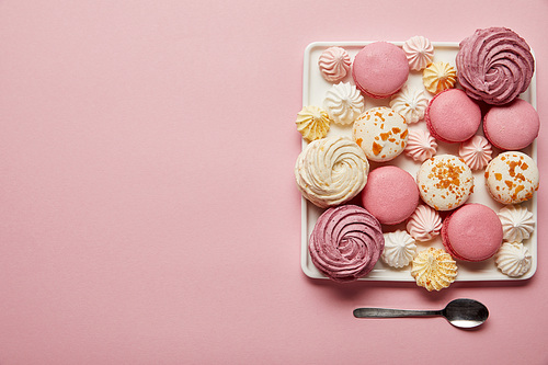 Flat lay with assorted meringues and macaroons on square dish with spoon on pink background
