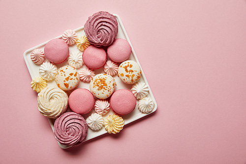 Top view of assorted french macaroons and meringues on square dish on pink background