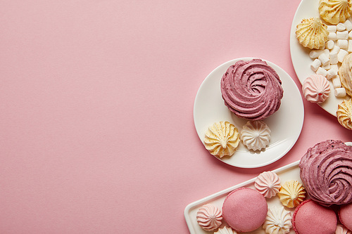 Top view of pink, white and yellow meringues, macaroons and marshmallows on pink background