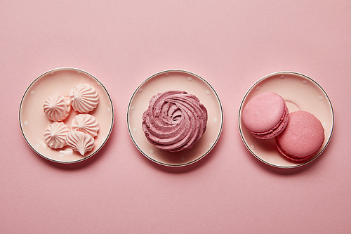 Flat lay with pink meringues and macaroons on pink dotted saucers on pink background