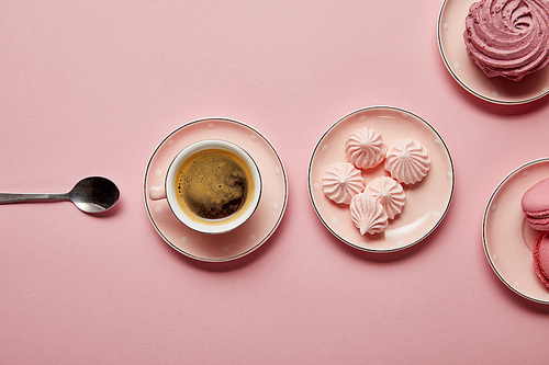 Top view of pink meringues and macaroons on pink dotted saucers with spoon and cup of coffee on pink background