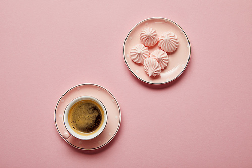 Top view of small pink meringues on dotted saucer and cup of coffee on pink background