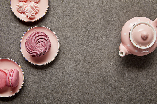 Top view of pink teapot and saucers with meringues and pink zephyr on gray background