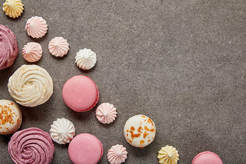 Top view of small meringues, pink and white macaroons and pink soft zephyr on gray background
