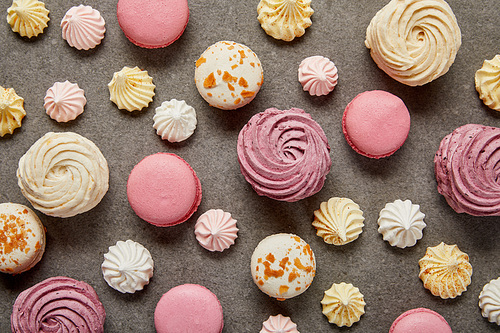 Top view of assorted pink white and yellow macaroons with meringues on gray background
