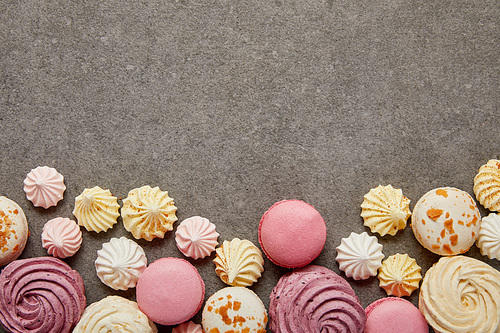 Top view of pink and white macaroons with pink, yellow and white meringues on gray background